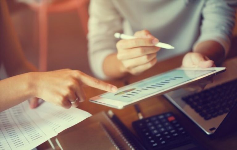 Two people are sitting at a table with papers and pens.